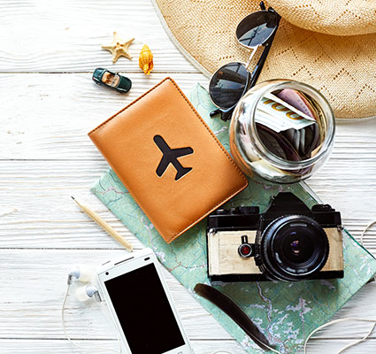 Travel items like map, camera, phone, journal, sunglasses on a wooden table.