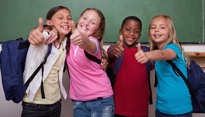 Image of kids smiling with backpacks on.